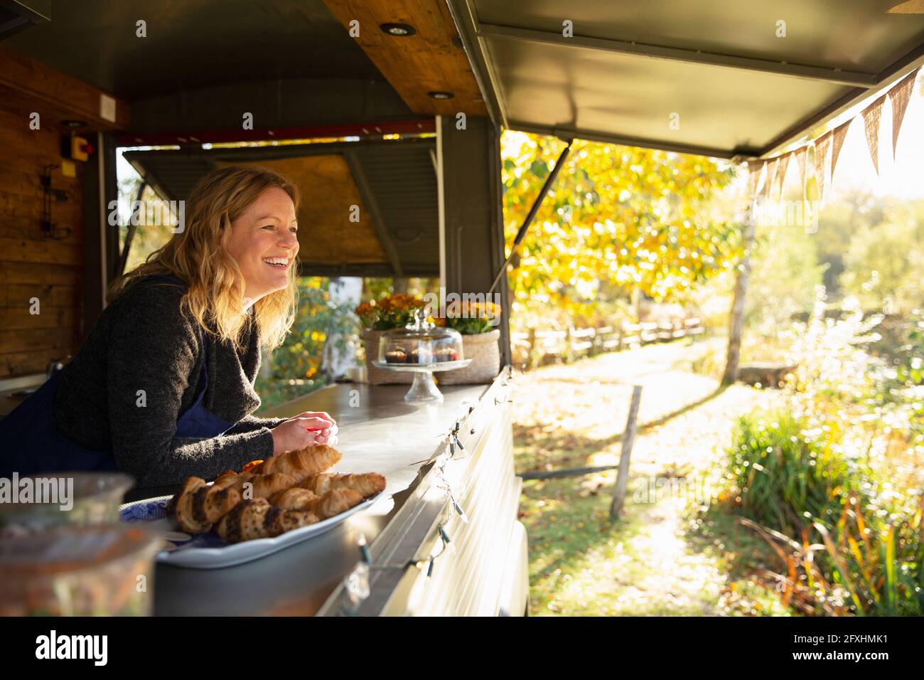Felice donna proprietario di carrello alimentare nel soleggiato parco autunnale Foto Stock