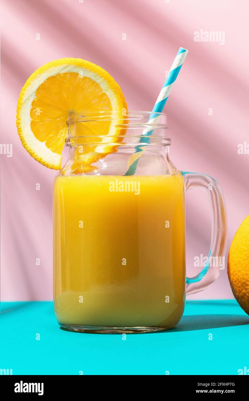 Succo d'arancia in un bicchiere con una paglia e un arancio su uno sfondo colorato, primo piano. Foto Stock