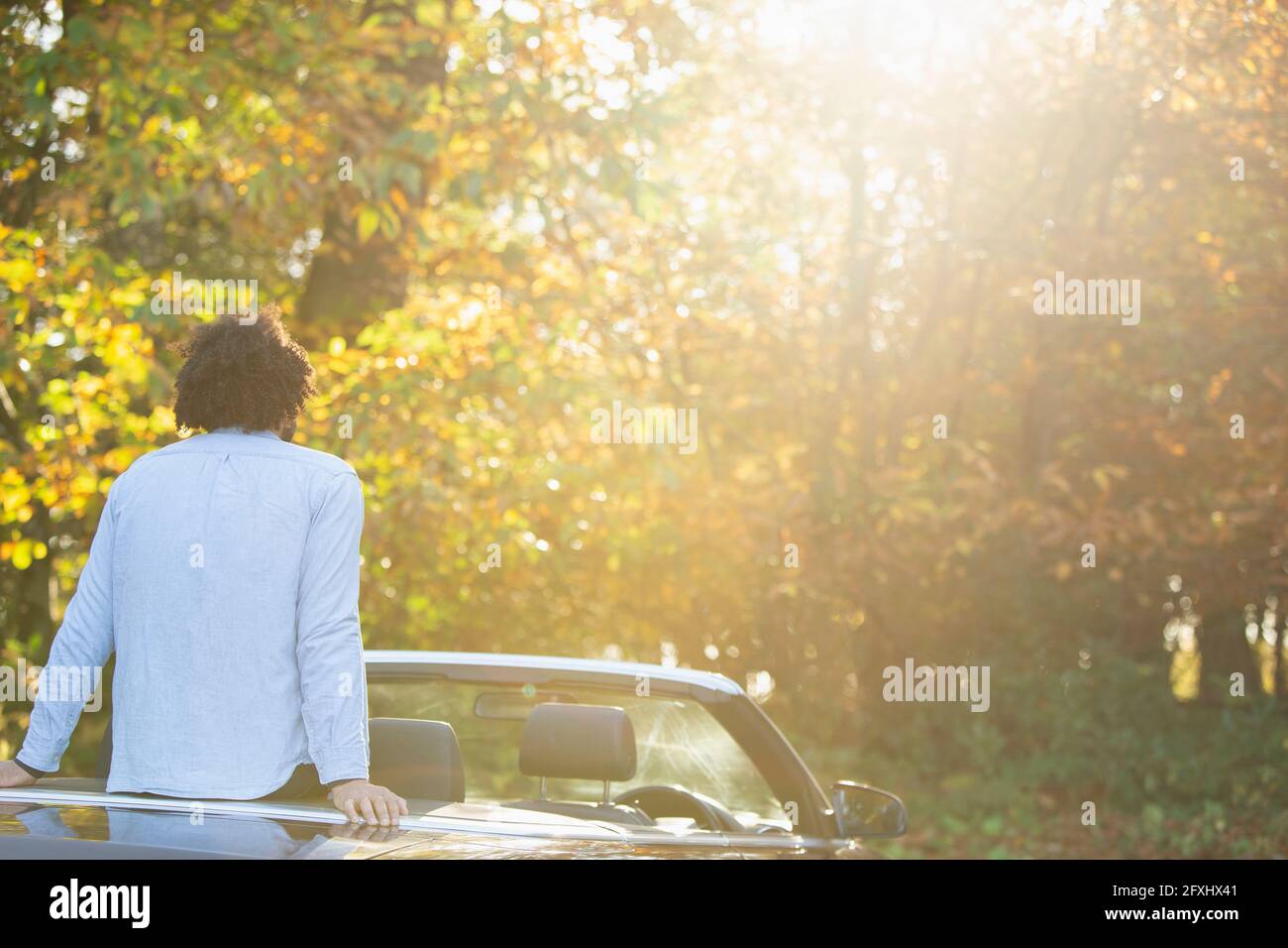 Giovane uomo in convertibile rilassante godendo di alberi soleggiati del parco autunnale Foto Stock