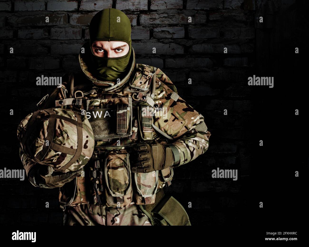 Foto di un soldato swat completamente attrezzato in munizioni pesanti di livello 3 e fucile in piedi su sfondo di mattoni scuri. Foto Stock
