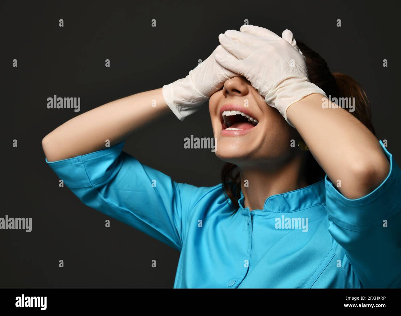 Allegra donna medico ginecologo riprodottista in guanti bianchi in lattice e. uniforme blu in piedi e coprendo gli occhi con le mani Foto Stock