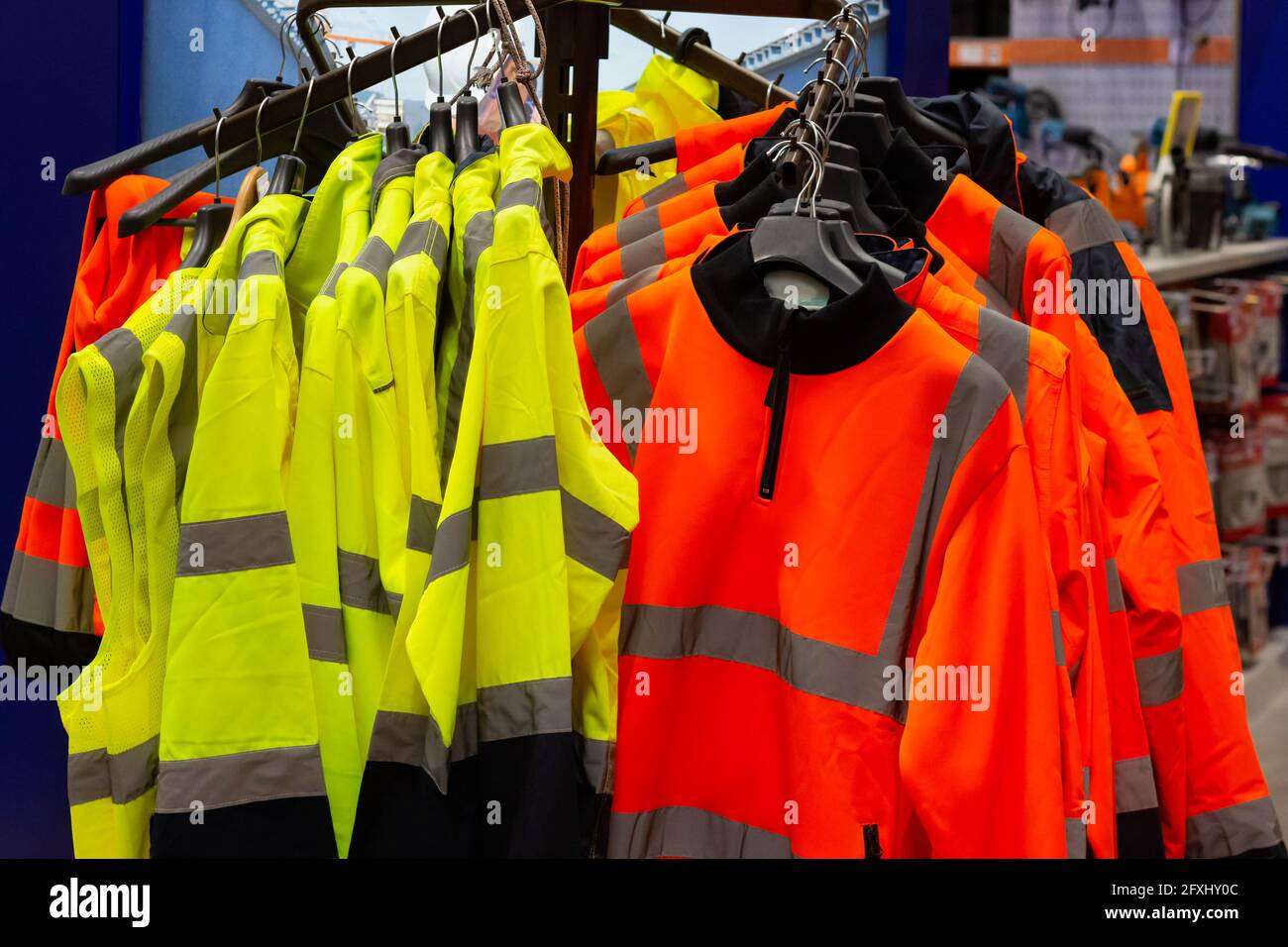 Foto di varie giacche di segnalazione colorate appese sul rack sullo scaffale del magazzino dei materiali da costruzione. Foto Stock