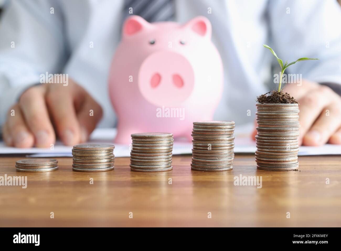 Le torri a moneta ascendenti si trovano sul tavolo contro lo sfondo di una banca di piggy rosa. Foto Stock