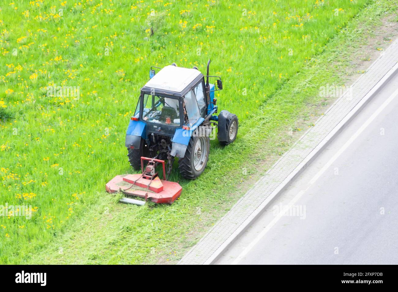 Il trattore utilizza il rasaerba trainato per falciare l'erba sui prati della città, vista aerea Foto Stock