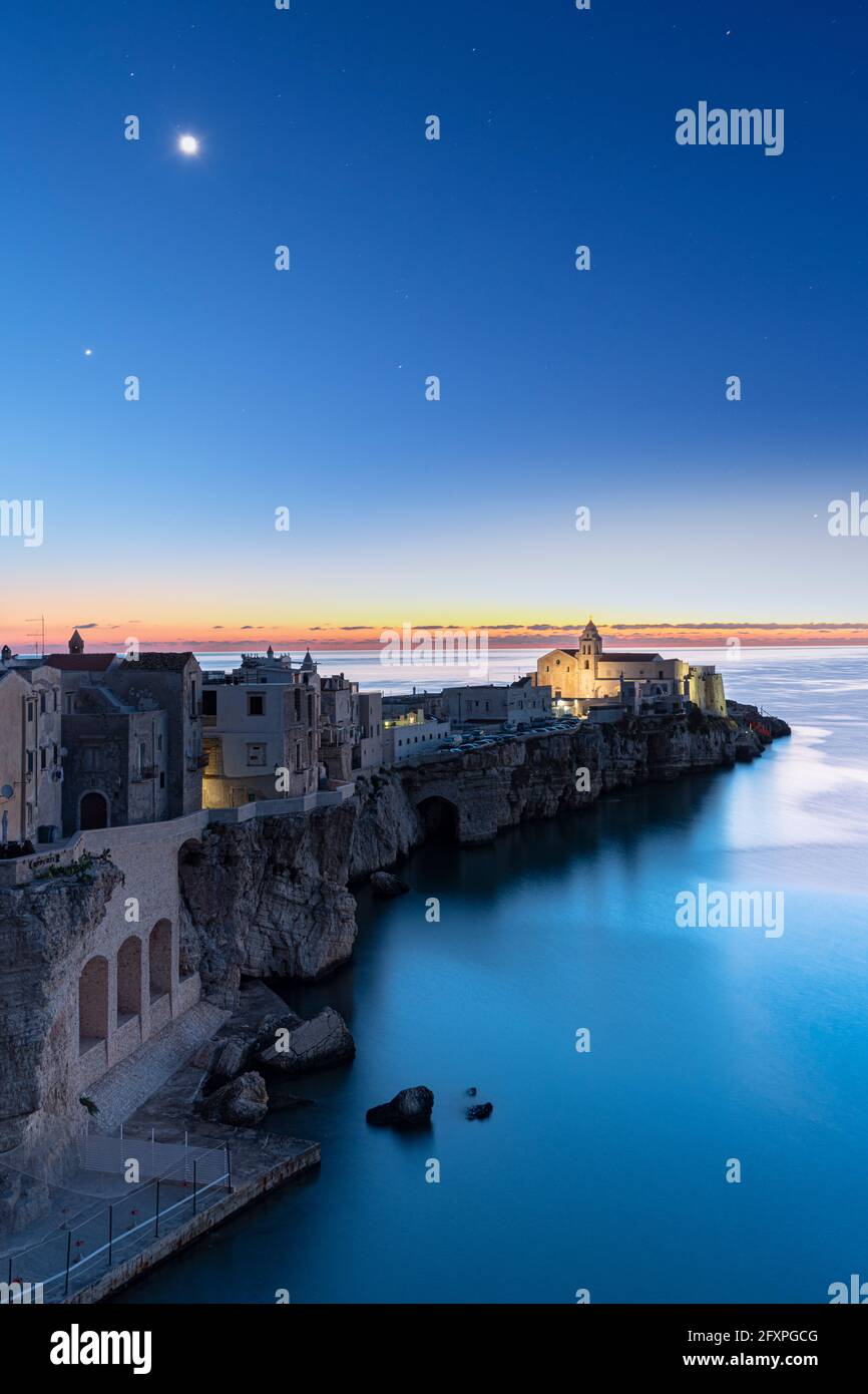 Vecchi edifici e la chiesa di Vieste illuminata dalla luna al tramonto, Vieste, provincia di Foggia, Parco Nazionale del Gargano, Puglia, Italia, Europa Foto Stock