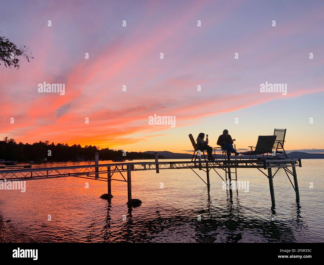 Madre e figlia suonano insieme ukulele su un molo sul lago Sebago, Maine, Stati Uniti d'America, Nord America Foto Stock