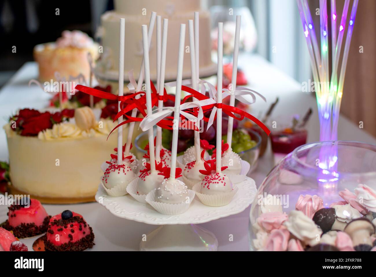 Pops sul tavolo di nozze. Papi in cioccolato bianco decorato con nastri rossi e bianchi. Dolce tavolo da nozze Foto Stock