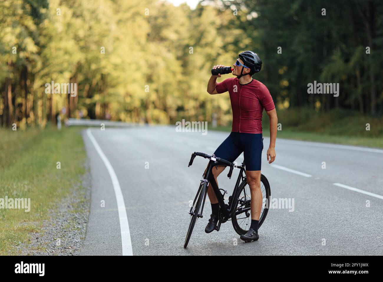 Giovane seduto in bicicletta e bevendo acqua dolce Foto Stock