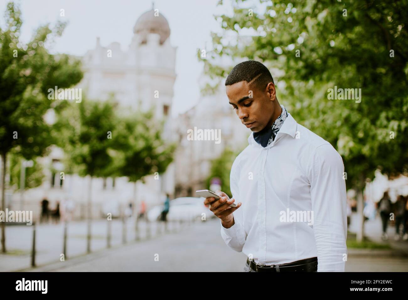Bel giovane uomo d'affari afro-americano che usa un telefono cellulare mentre attesa di un taxi in attesa di un taxi su una strada Foto Stock