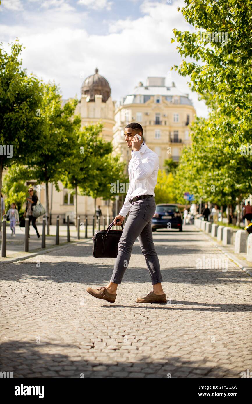 Bel giovane uomo d'affari afro-americano che usa un cellulare su una strada Foto Stock