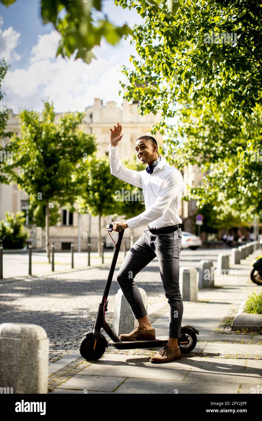 Bel giovane afroamericano con scooter elettrico su una strada Foto Stock