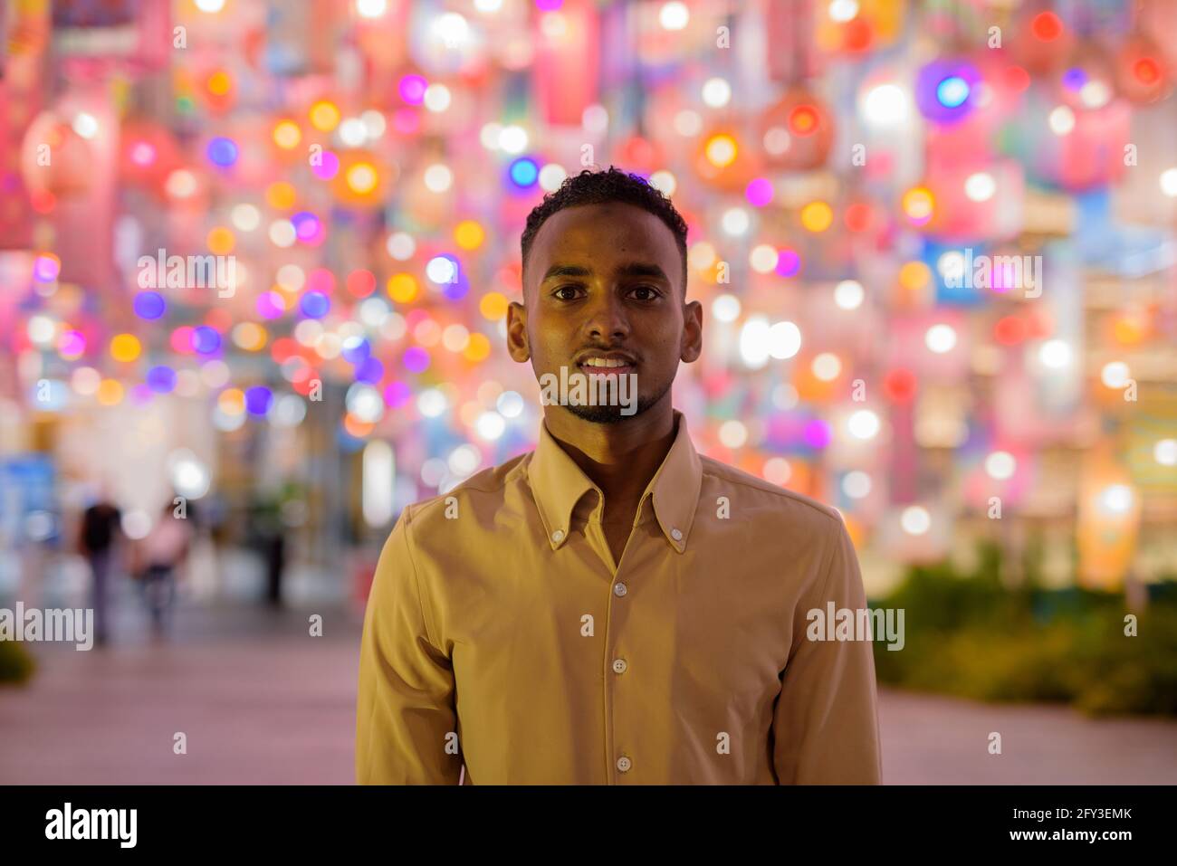 Giovane uomo d'affari nero sorridente all'aperto in città di notte con luci a lanterna colorate Foto Stock