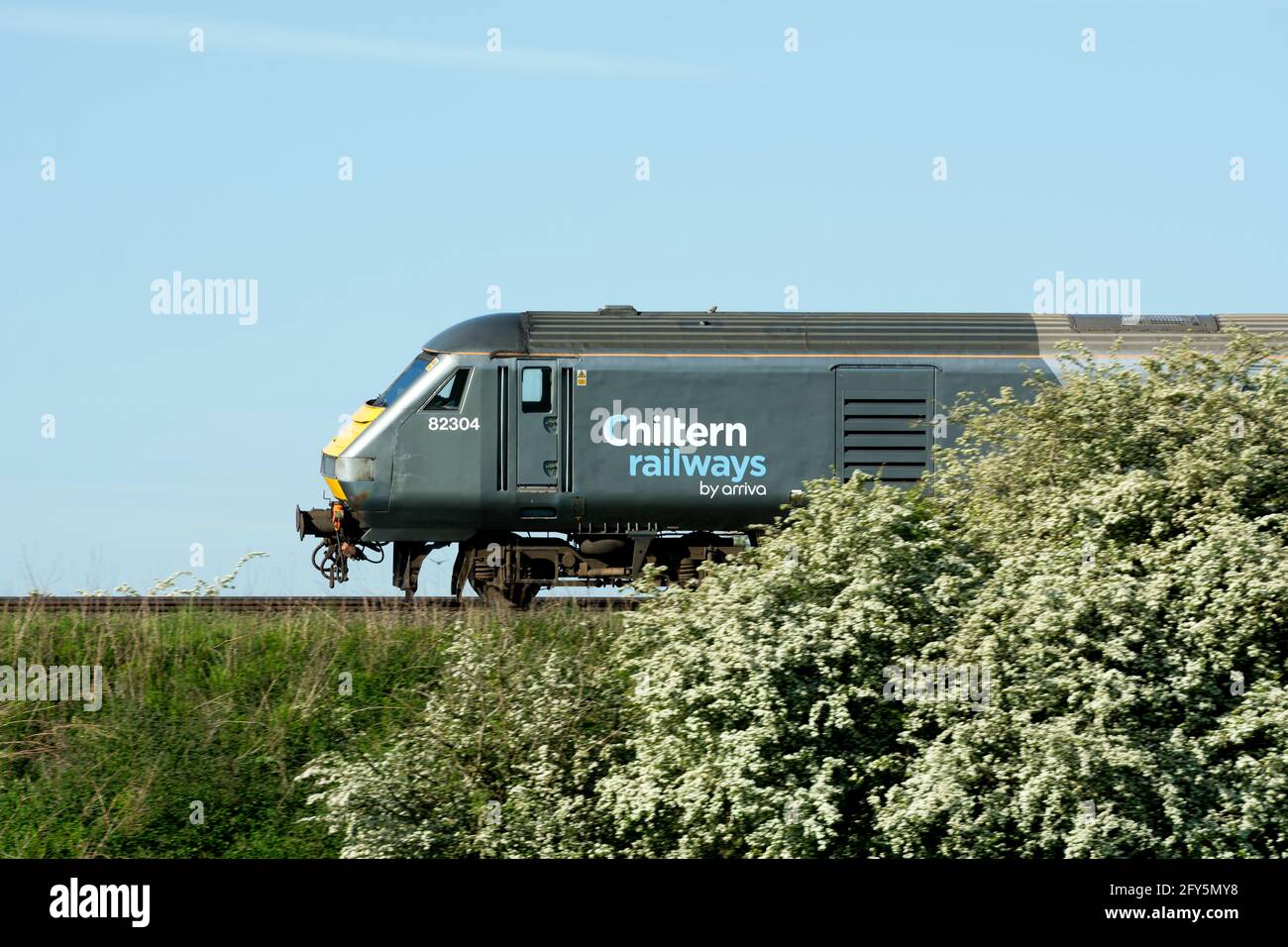 Un treno della linea principale Chiltern Railways, vista laterale, e Hawthorn Blossom in primavera, Warwickshire, Regno Unito Foto Stock