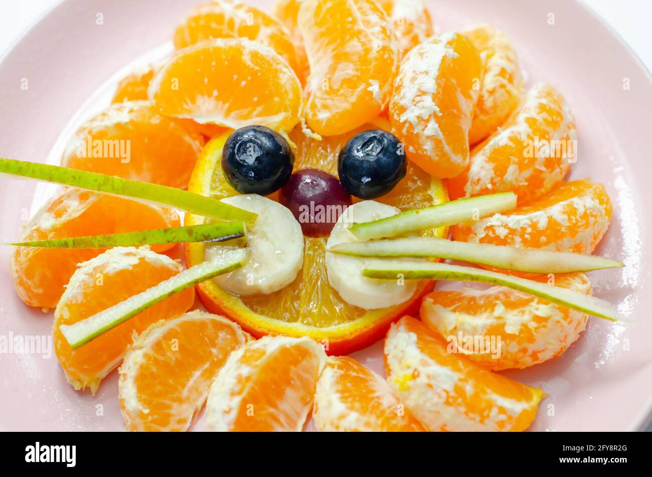 Frutta fresca, arancio, mandarino, banana, uva e pera serviti in modo creativo, spuntino a base di leoni, cibo divertente Foto Stock