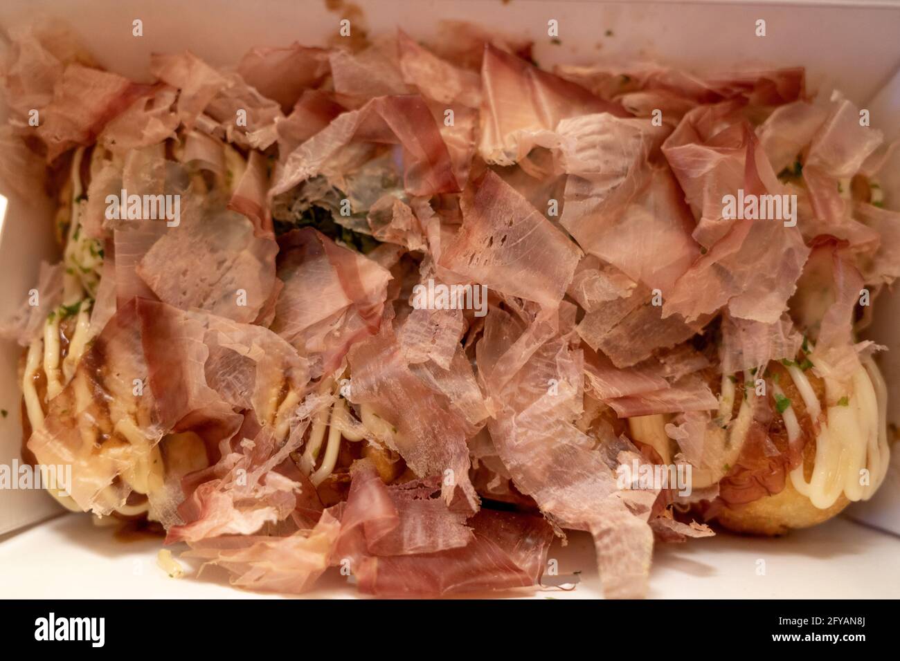 Primo piano e vista macro al katsuobushi, fiocco di bonito che sulla cima di Takoyaki o polpo giapponese palle, servire su scatola di carta bianca. Foto Stock