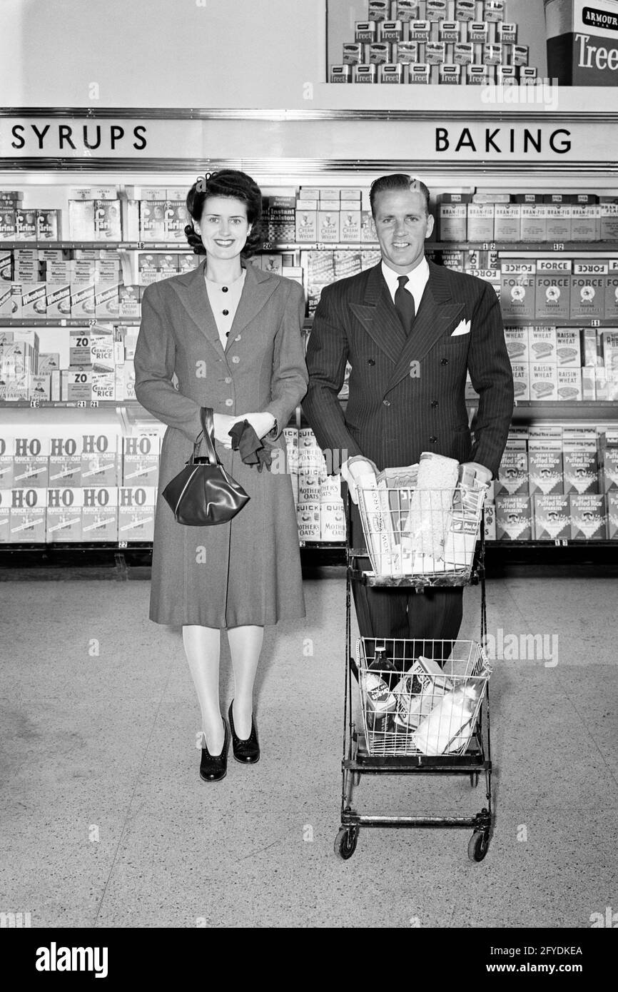 1940 UOMO E DONNA COPPIA SHOPPING IN NEGOZIO DI ALIMENTARI UOMO CARRELLO DI SPESA DI SPINTA - S11552 HAR001 HARS ESPRESSIONE TEMPO VECCHIO NOSTALGIA OCCUPATO VECCHIA MODA 1 STUPIDO VISO GIOVANE ADULTO FUMETTO LAVORO DI SQUADRA FELICE GIOIA STILE DI VITA FEMMINE SPOSATO CONIUGE MARITI COPIA SPAZIO A LUNGHEZZA INTERA SIGNORE PERSONE NEGOZI MASCHI ESPRESSIONI B&W PARTNER SHOPPER EYE CONTATTA IL TUTA DELLO SHOPPING E LEGARE DIVERTENTE SCOPERTA E SCELTA ALLEGRA I SORRISI COMICI IMMAGAZZINA LA COMMEDIA CONCETTUALE GIOIOSA COMMERCIO ELEGANTE DEL POCKETBOOK TOGETHERNESS MOGLI GIOVANE UOMO ADULTO GIOVANE DONNA ADULTO NERO E BIANCO AZIENDE ETNIA CAUCASICA HAR001 VECCHIO STILE Foto Stock
