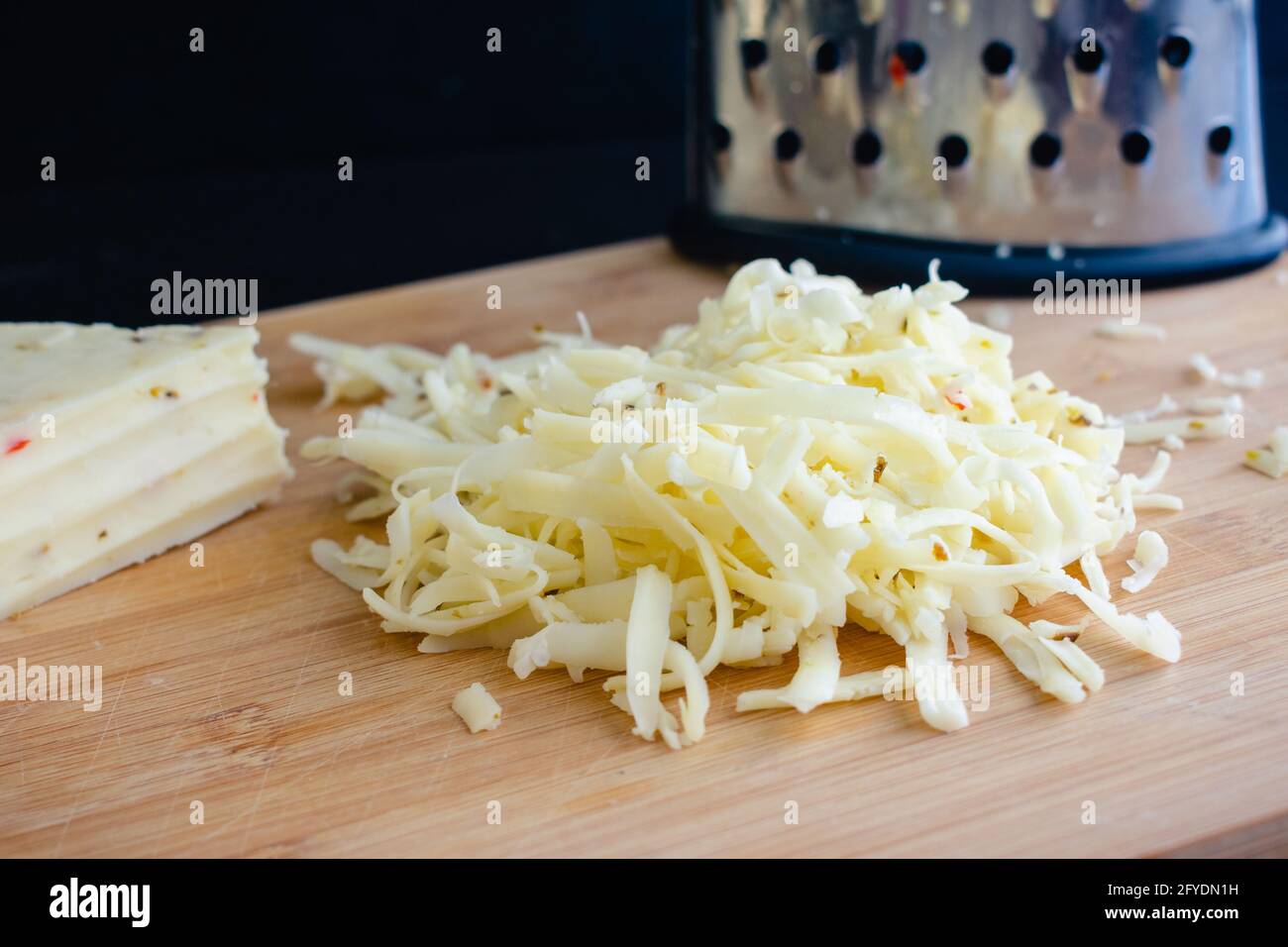 Formaggio di Jack del peperone grattugiato: Formaggio grattugiato e una grattugia della scatola su un tagliere di bambù Foto Stock