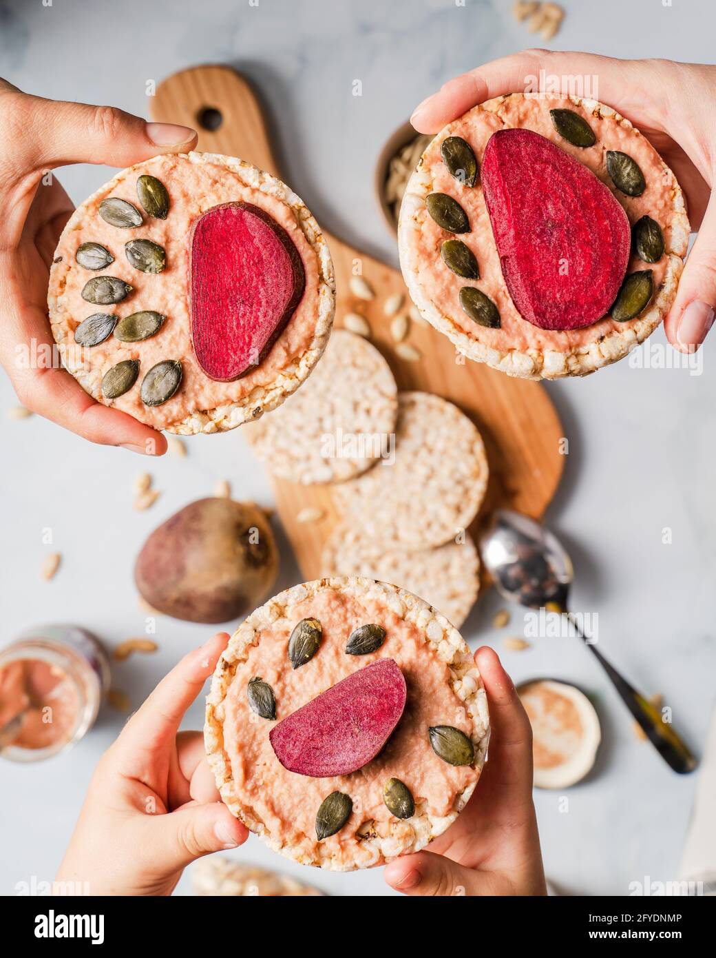 Croccanti torte di riso soffiato sul tavolo hummus spalmato e pomodoro e verdure di barbabietola e semi di zucca di sesamo sulla tavola - vista dall'alto su mani che tengono healt Foto Stock