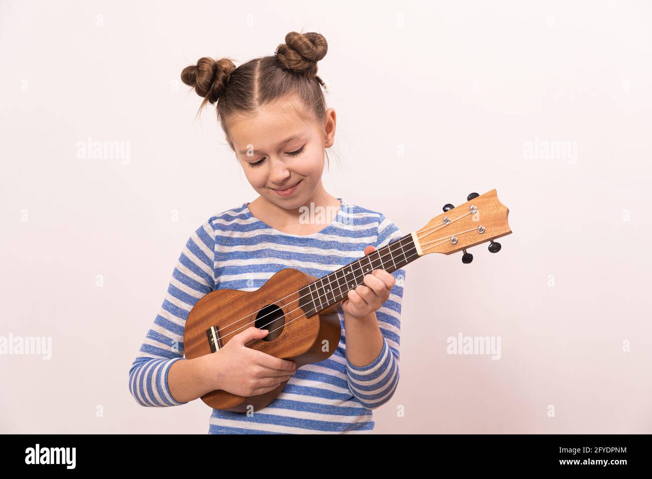 La ragazza canta e suona l'ukulele. Il bambino ride, si pone per la macchina fotografica e gode la musica. Imparare a giocare ukuleles. Foto Stock