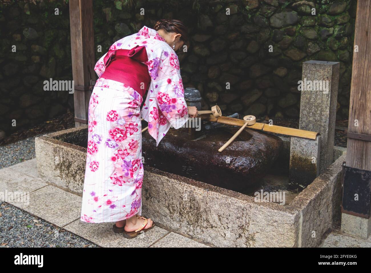 Kyoto, Giappone - 15 settembre 2017: Donna in kimono che sciacqua le mani alla fontana giapponese purifica dell'acqua, chiamata chozubachi, al santuario di Fushimi Inari Taisha Foto Stock