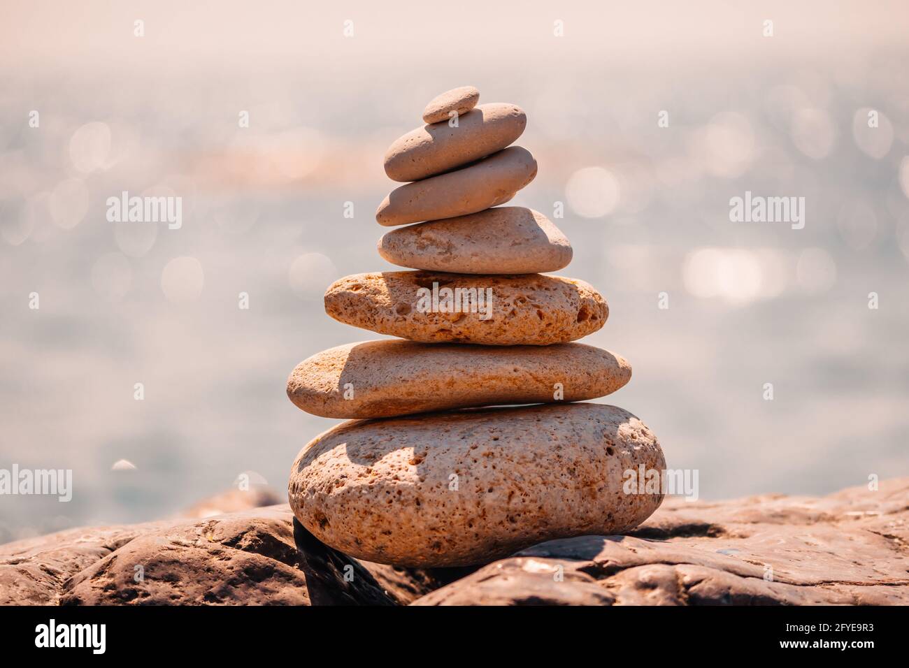 Equilibrata piramide di ciottoli sulla spiaggia in una giornata di sole. Abstract Sea bokeh sullo sfondo. Messa a fuoco selettiva. Pietre Zen sulla spiaggia di mare, meditazione Foto Stock