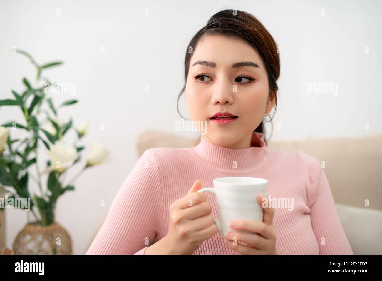 Ripresa interna di una donna asiatica sorridente che beve tè. Foto Stock