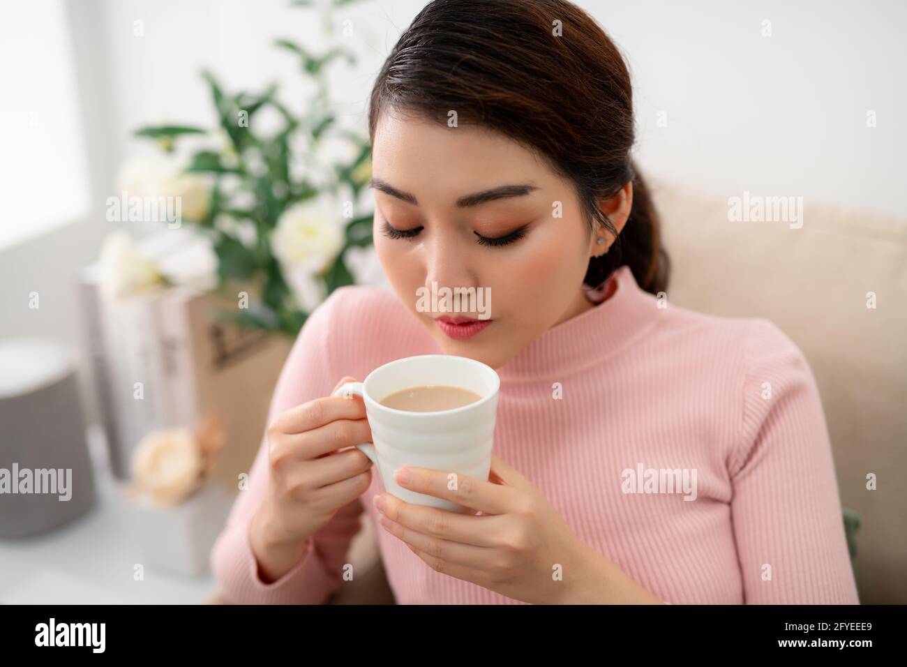 Ripresa interna di una donna asiatica sorridente che beve tè. Foto Stock
