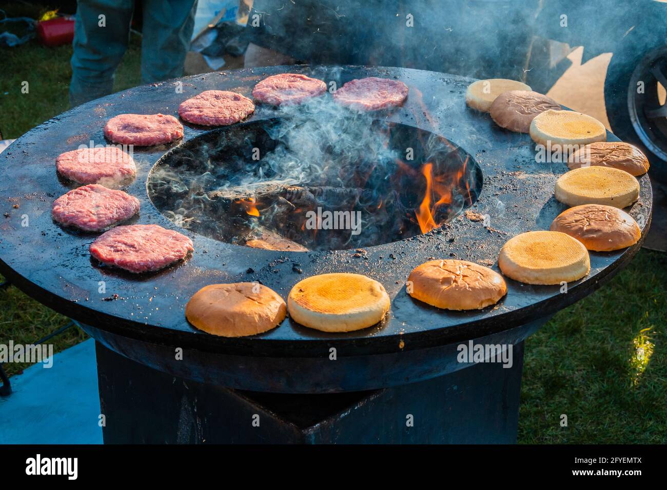 Le polpettine di manzo e gli hamburger sono grigliati su una grande griglia rotonda a legna all'aperto. Festa del barbecue nel parco cittadino. Street fast food. Foto Stock