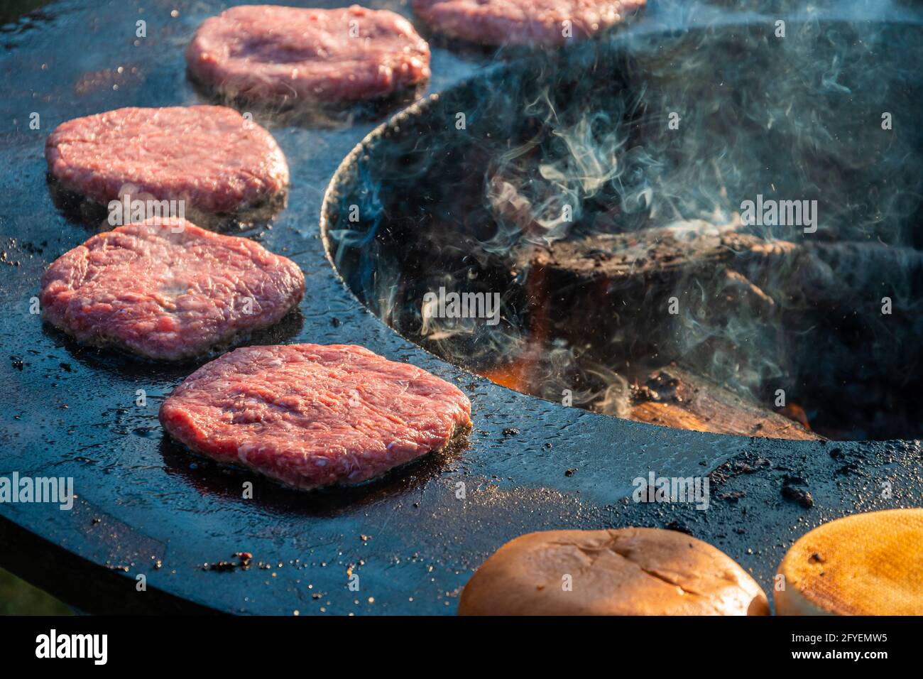 Le polpettine di manzo e gli hamburger vengono grigliati su una grande griglia rotonda all'aperto che brucia il legno, primo piano. Festa del barbecue nel parco cittadino. Via veloce Foto Stock