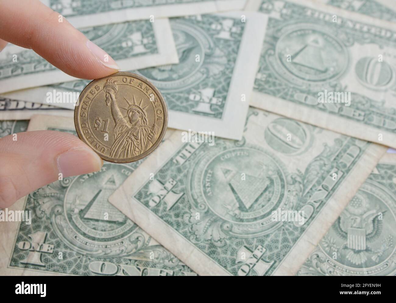Mano tagliata che tiene una moneta del dollaro uno noi nel sfondo di molti uno us dollari note Foto Stock