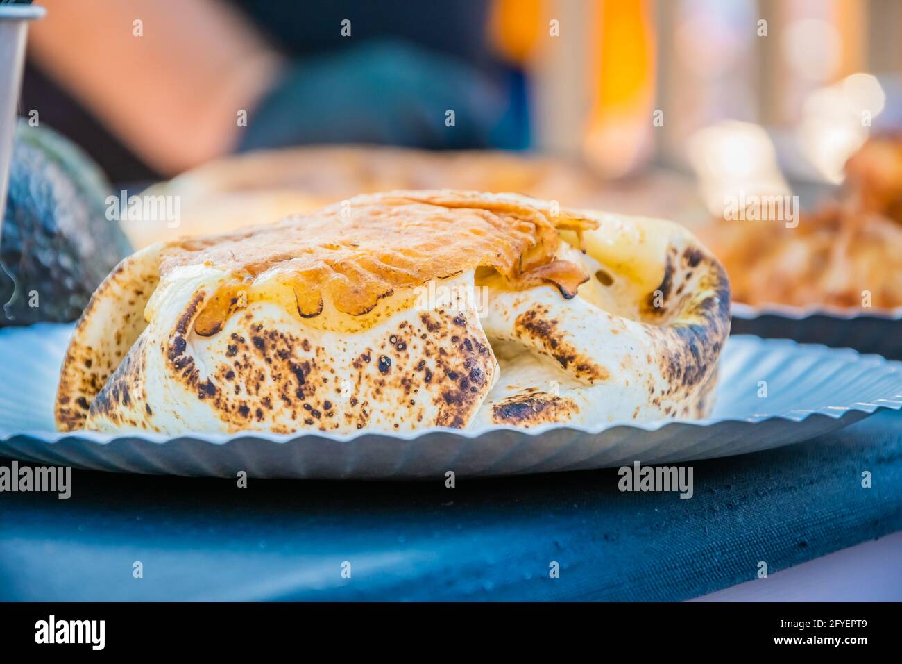 Cibo messicano, un hamburger di bistecca avvolto in una tortilla sotto il formaggio fuso al banco di un ristorante all'aperto. Festa del cibo nel parco cittadino. Via Foto Stock