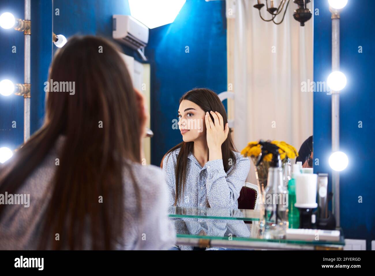 Una donna che guarda se stessa nello specchio alla bellezza salone Foto Stock