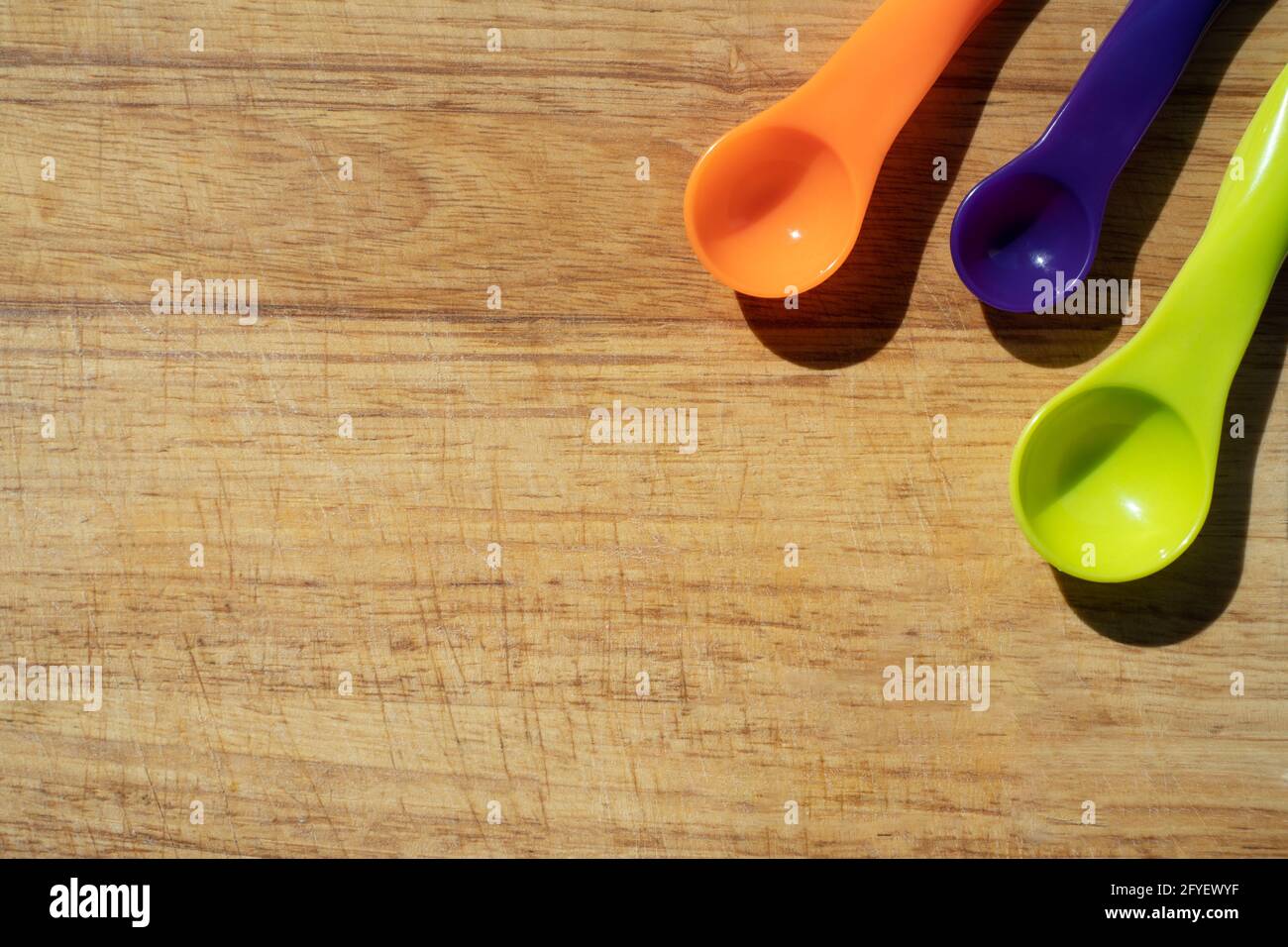 Usato tagliere da cucina in legno con colorati cucchiai di misurazione in angolo. Vista dall'alto del banner Foto Stock