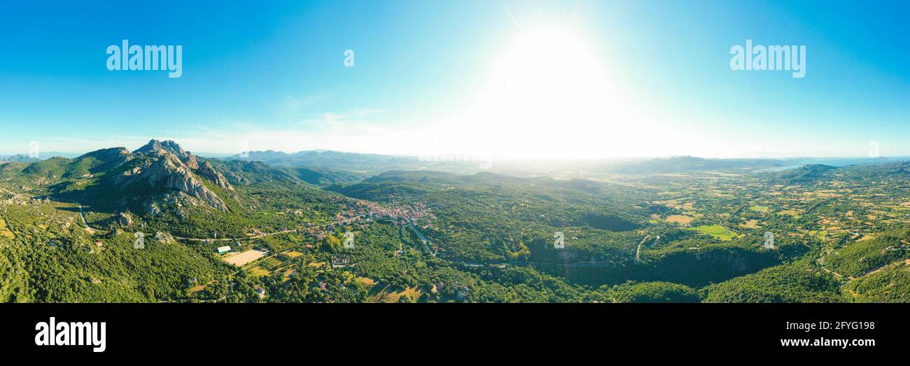 Vista dall'alto, splendida vista aerea del villaggio di San Pantaleo circondato da alcune montagne di granito, vegetazione verde e il Mar mediterraneo Foto Stock
