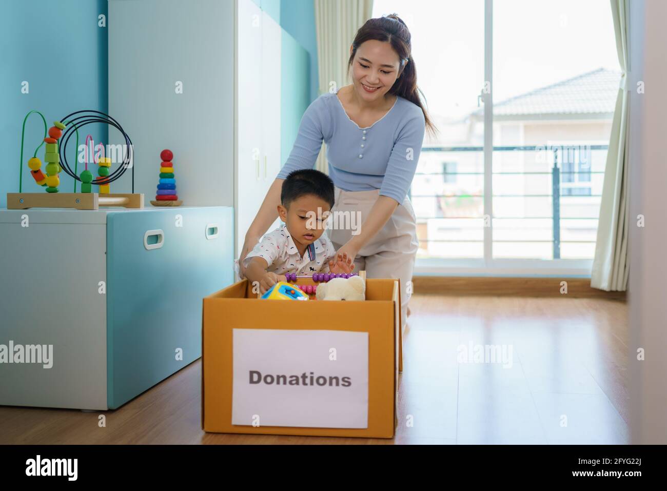 La madre e il figlio asiatici stanno scegliendo i giocattoli dei loro bambini che non stanno giocando e mettendo le scatole di donazione al centro di donazione. Foto Stock