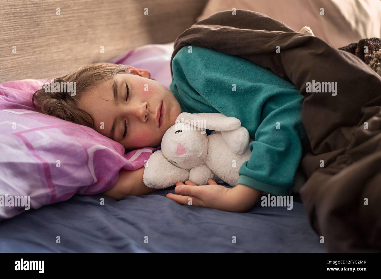 ragazzo dolce biondo che dormiva nel letto che regge un giocattolo Foto Stock