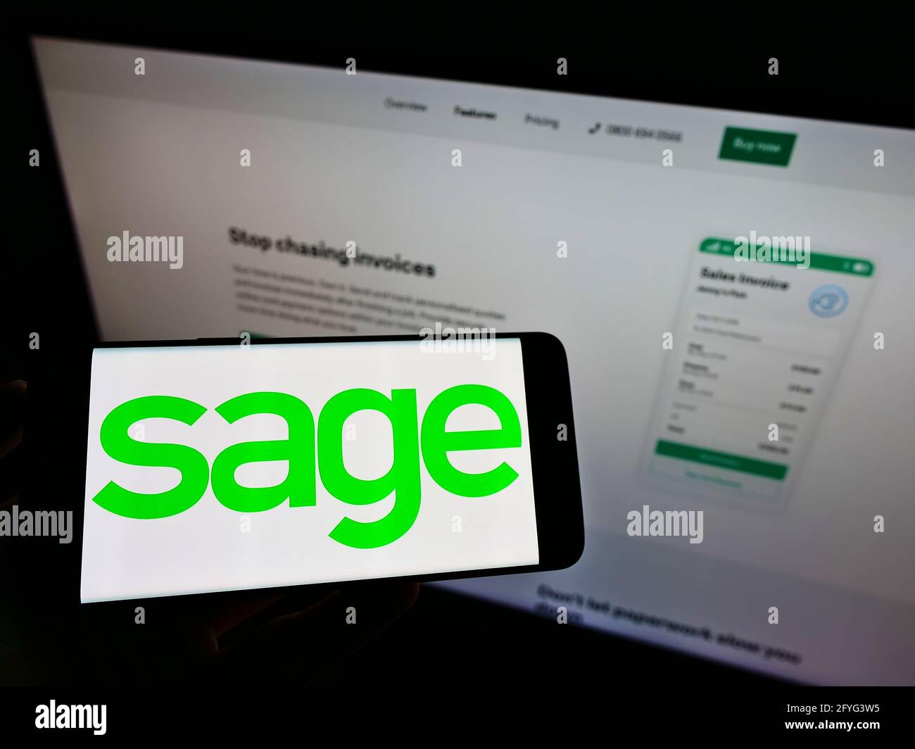 Persona che tiene il cellulare con il logo della società di software britannica il gruppo di Sage plc sullo schermo davanti alla pagina web di affari. Mettere a fuoco il display del telefono. Foto Stock