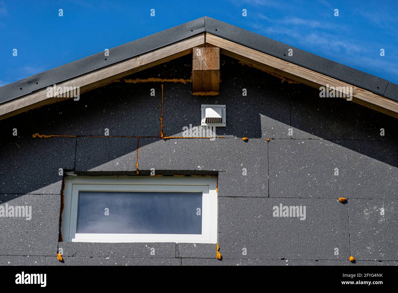 Una griglia di ventilazione in plastica sulla facciata dell'edificio in polistirene isolante nero, posta sotto il traliccio del tetto. Foto Stock