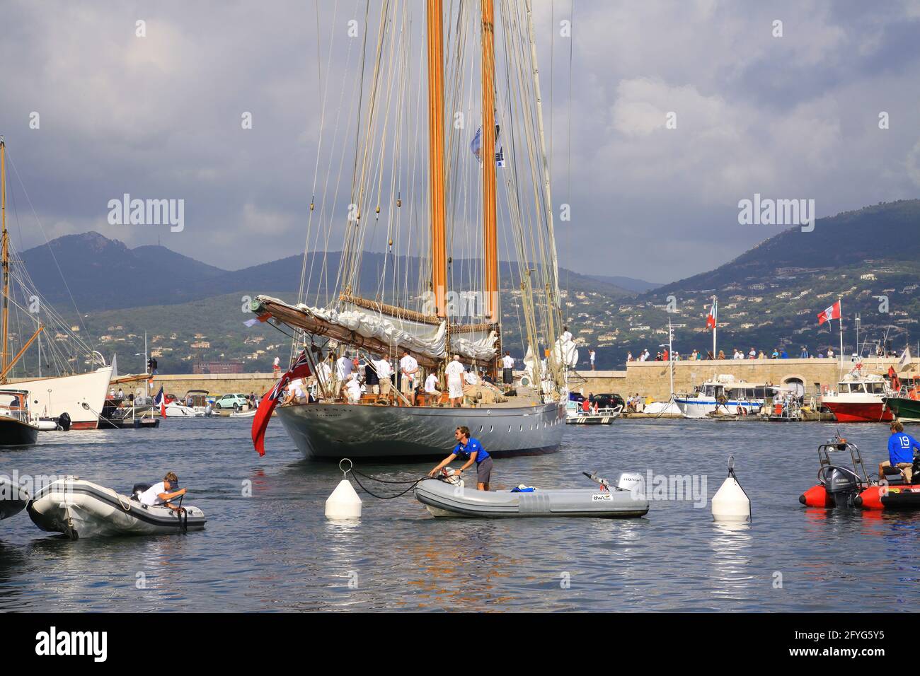 Saint Tropez - Francia - 3 ottobre. 2019: Vista sulla barca a vela con dinghies nella baia mediterranea durante regata, montagne e sfondo nuvole (Focus on Foto Stock