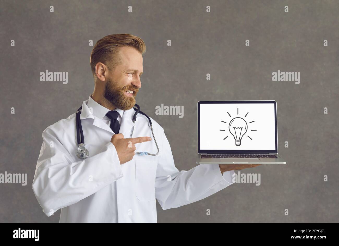 Il medico maschile punta a uno schermo di un laptop che ha una lampadina che è un simbolo di un'idea innovativa. Foto Stock