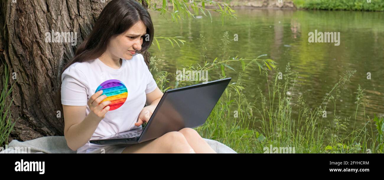 Una donna freelance o uno studente lavora in un computer portatile in natura e lo schiocca con un involucro a bolle riutilizzabile. Luogo di intestazione per il testo Foto Stock