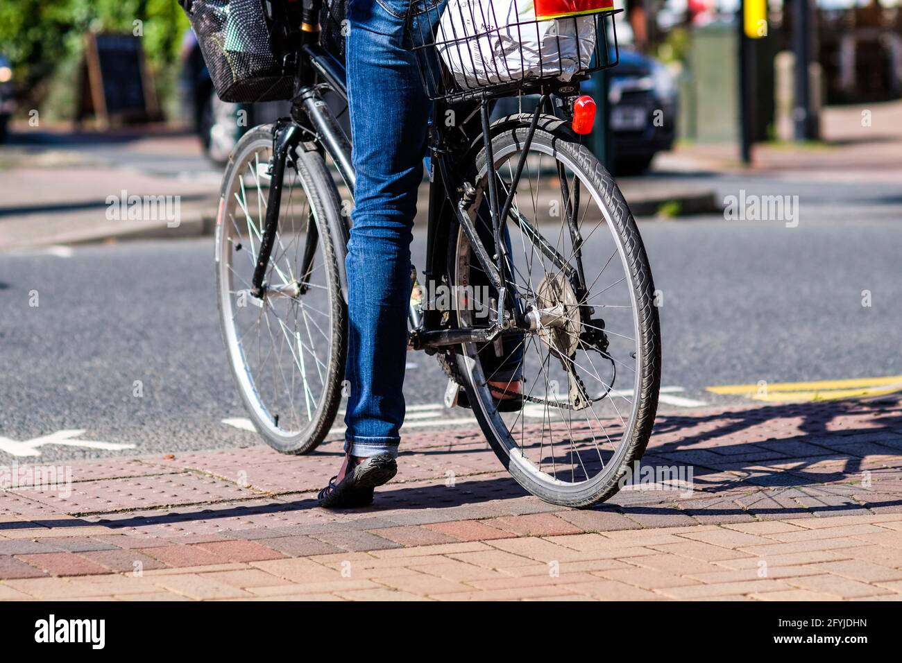 Una donna che indossa jeans blu sulla sua vecchia pedalata con un piede a terra, in attesa che il traffico si libera nel centro di town Foto Stock