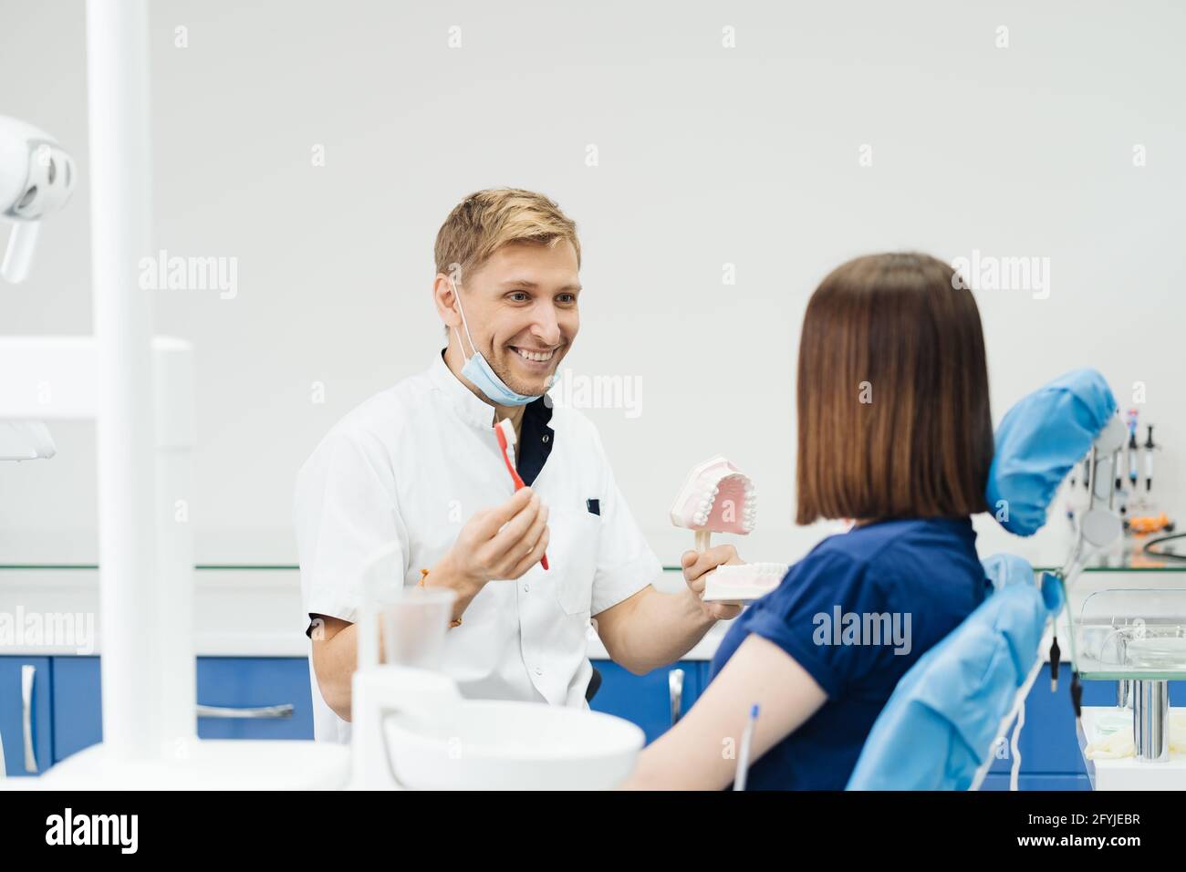 Dentista che mostra la corretta igiene dentale utilizzando mock-up di scheletro di denti. Medico stomatologo che spiega la corretta igiene dentale per il paziente che tiene un campione di mandibola umana con spazzolino da denti. Foto Stock
