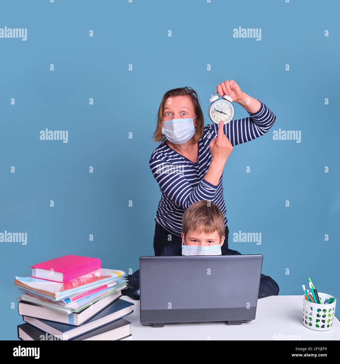 Madre di uno scolaro in una maschera medica viso mostra in tempo, una scuola scrivania su uno sfondo blu durante la pandemia coronavirus Foto Stock