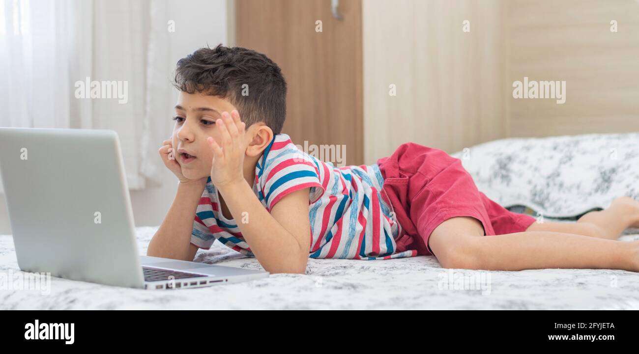 Bambino ragazzo sdraiato a letto usando un computer portatile. Lezione online sul video. Formazione remota a distanza. Nuovo studio scolastico normale. Bambini a scuola Foto Stock