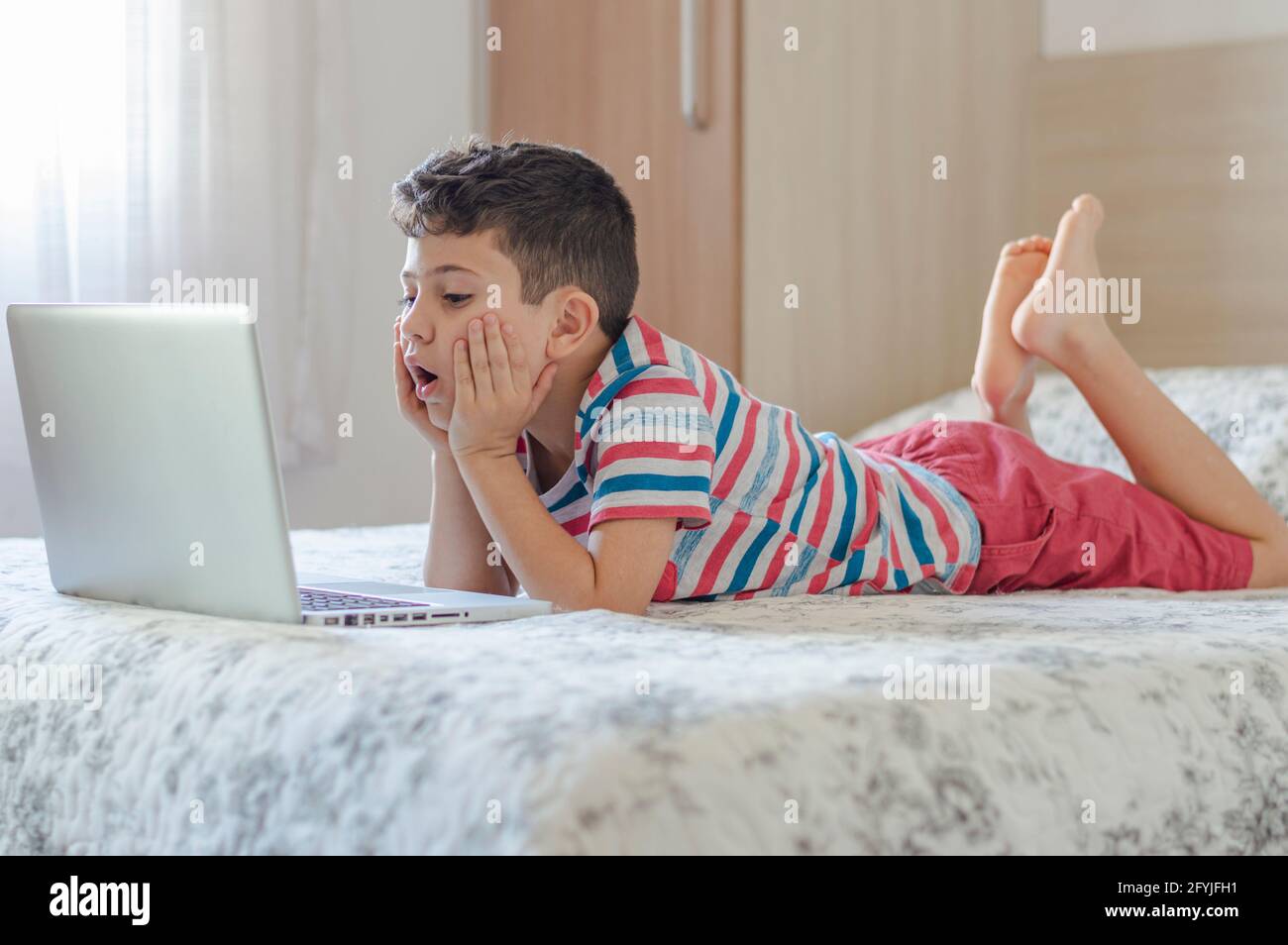 Bambino ragazzo sdraiato a letto usando un computer portatile. Lezione online sul video. Formazione remota a distanza. Nuovo studio scolastico normale. Bambini a scuola Foto Stock