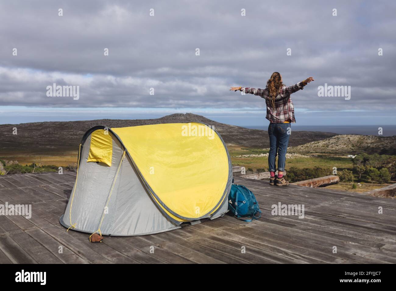 Vista posteriore del campeggio donna caucasica, in piedi fuori tenda sul ponte di montagna, braccia estese Foto Stock