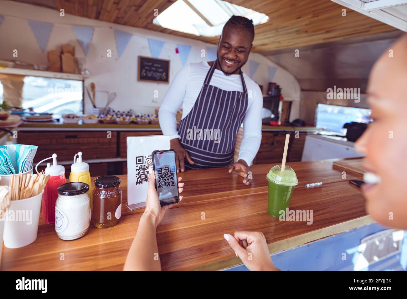 Sorridente afroamericano in camion di cibo con cliente femminile lettura del codice qr con lo smartphone Foto Stock