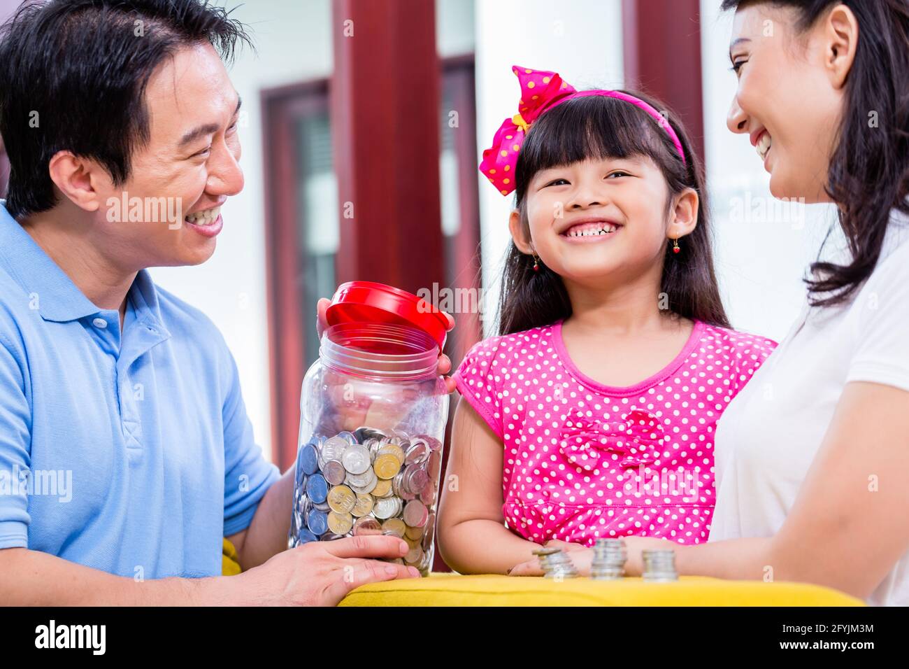 Famiglia cinese di risparmio di denaro per college fund del bambino, mettendo le monete in vaso Foto Stock