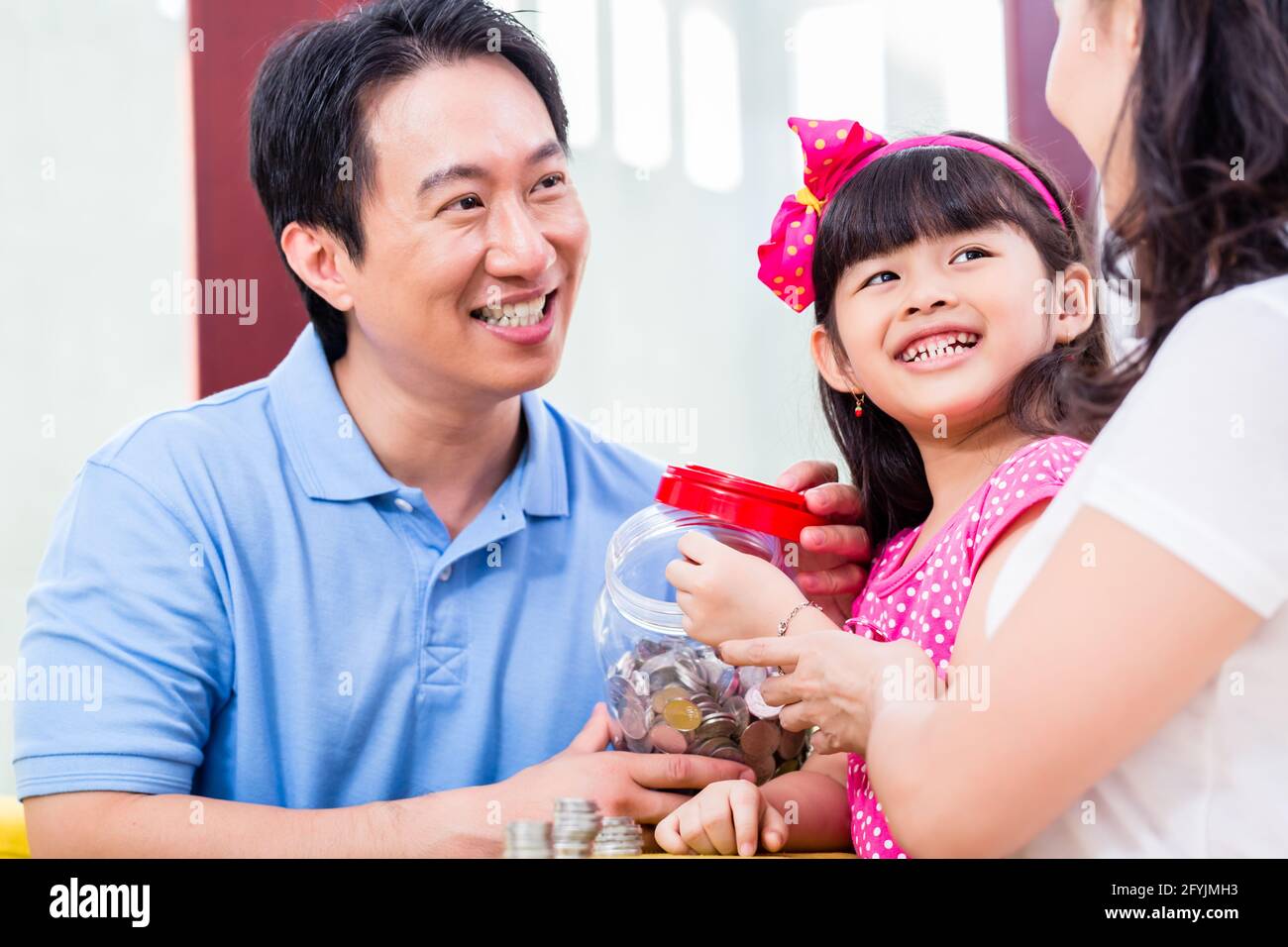 Famiglia cinese di risparmio di denaro per college fund del bambino, mettendo le monete in vaso Foto Stock
